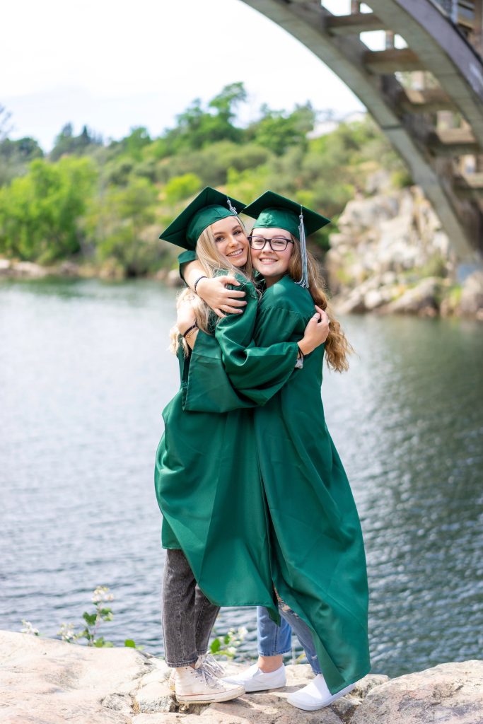 Two girls in their cap and gown smiling under a bridge.