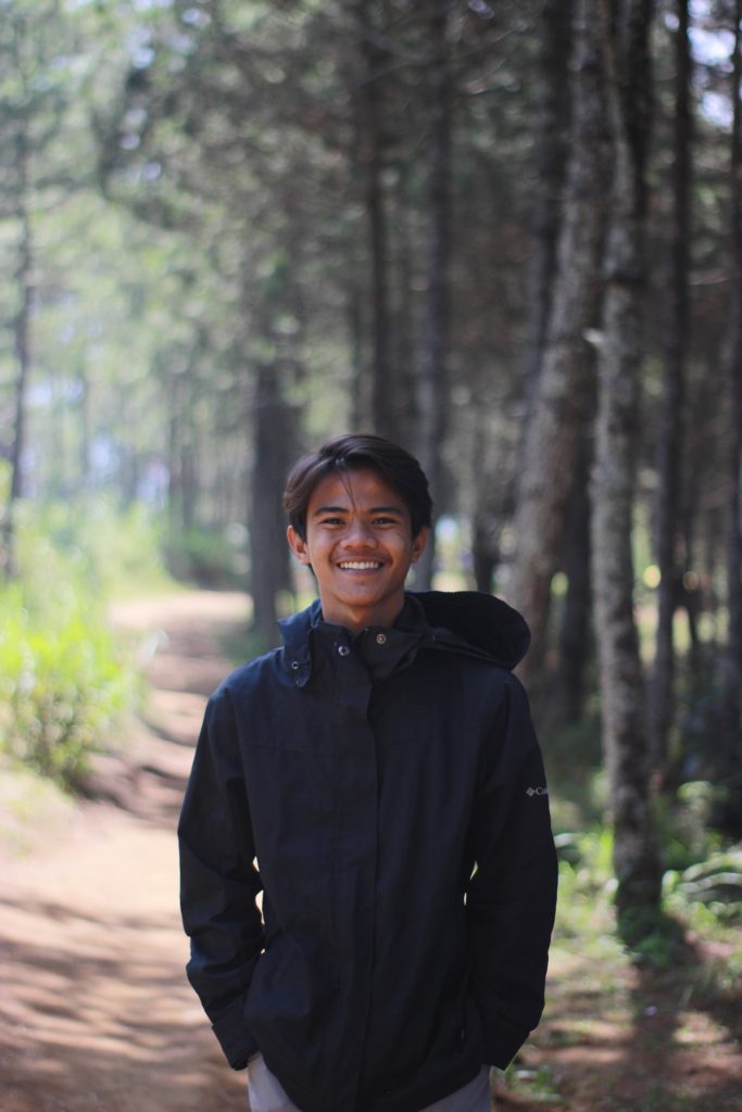 A picture of a man smiling in the woods.