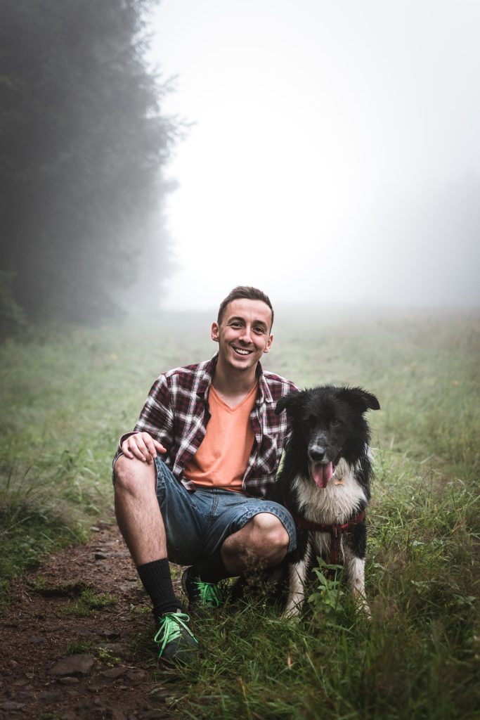 A man smiling with his dog in a misty field.